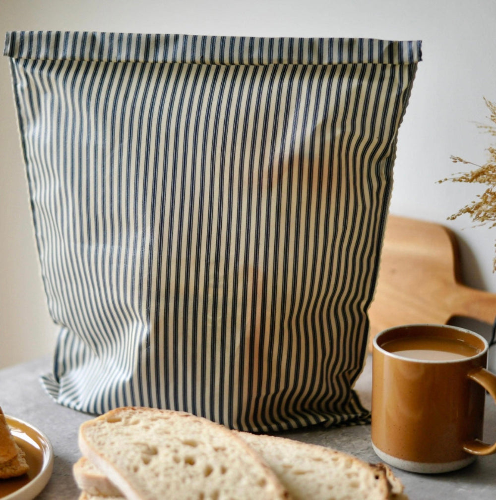 Striped bread bag on a table with bread slices and a mug of coffee.