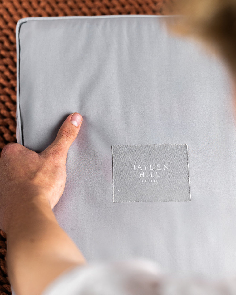 Grey organic cotton storage bag in the colour grey with 'Hayden Hill' label held by a hand on a textured surface