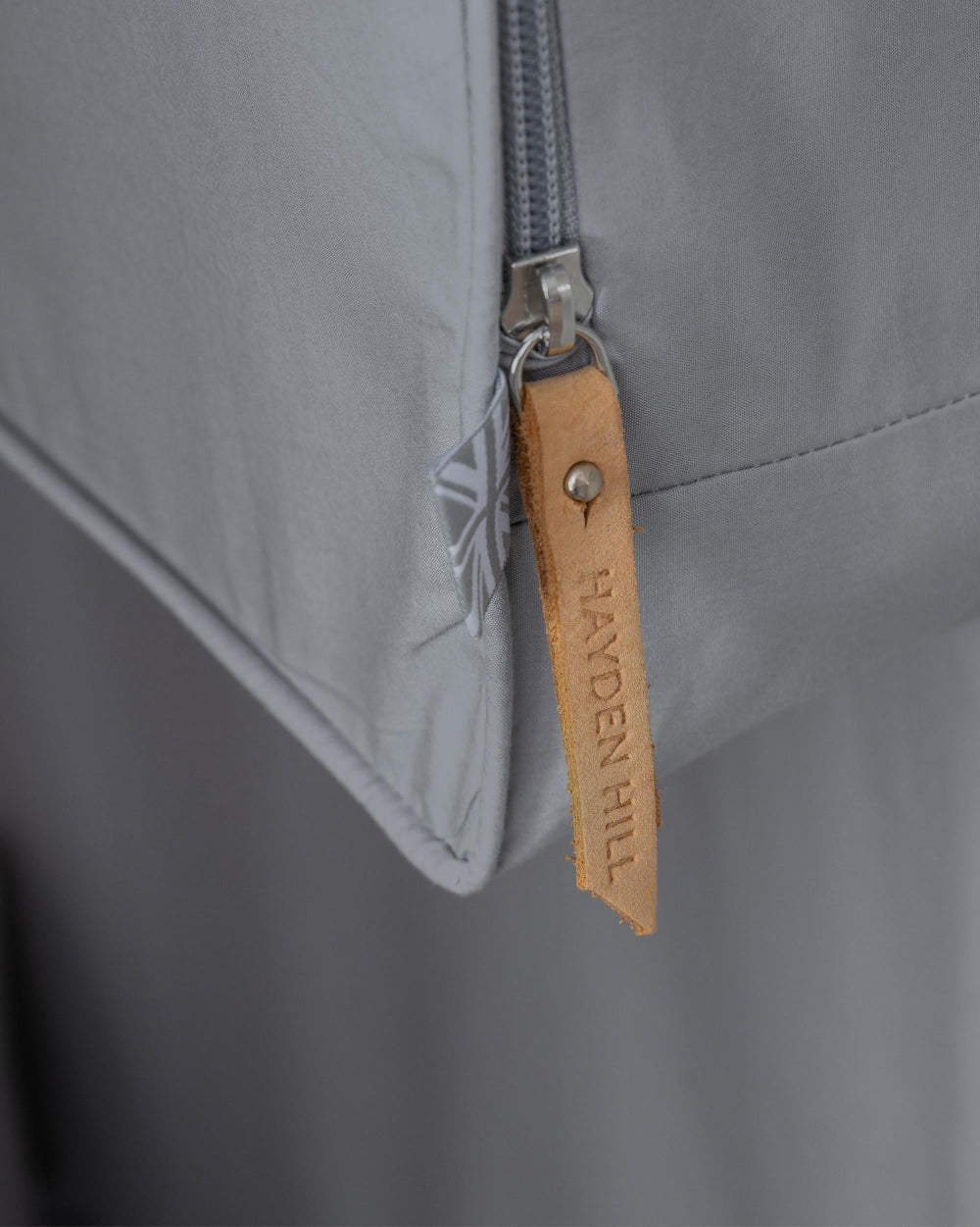 Close-up of a gray jacket with a leather union jack and zipper, featuring the brand 'Hayden Hill'.