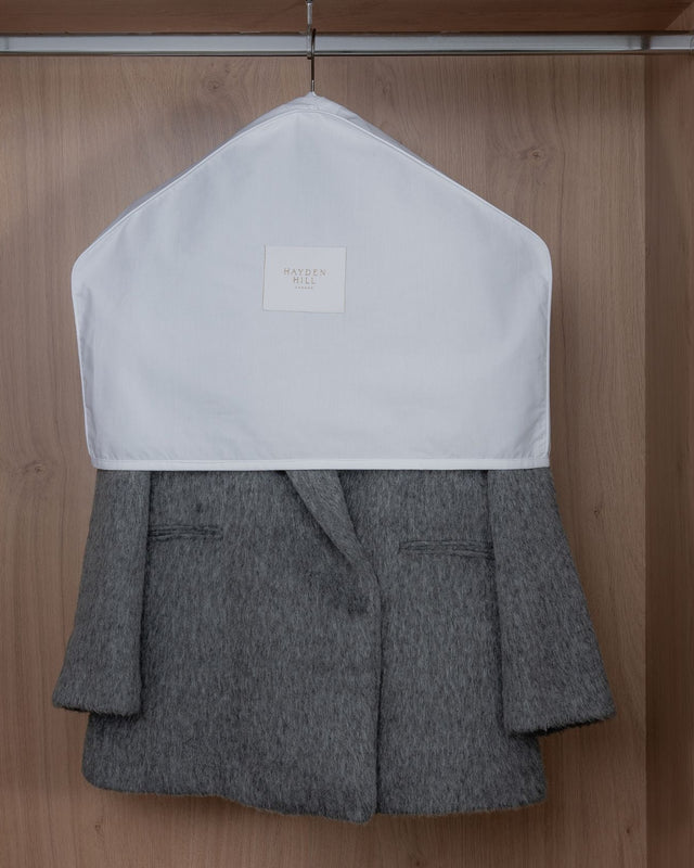 Grey blazer with white organic dust cover on shoulders on a wooden hanger