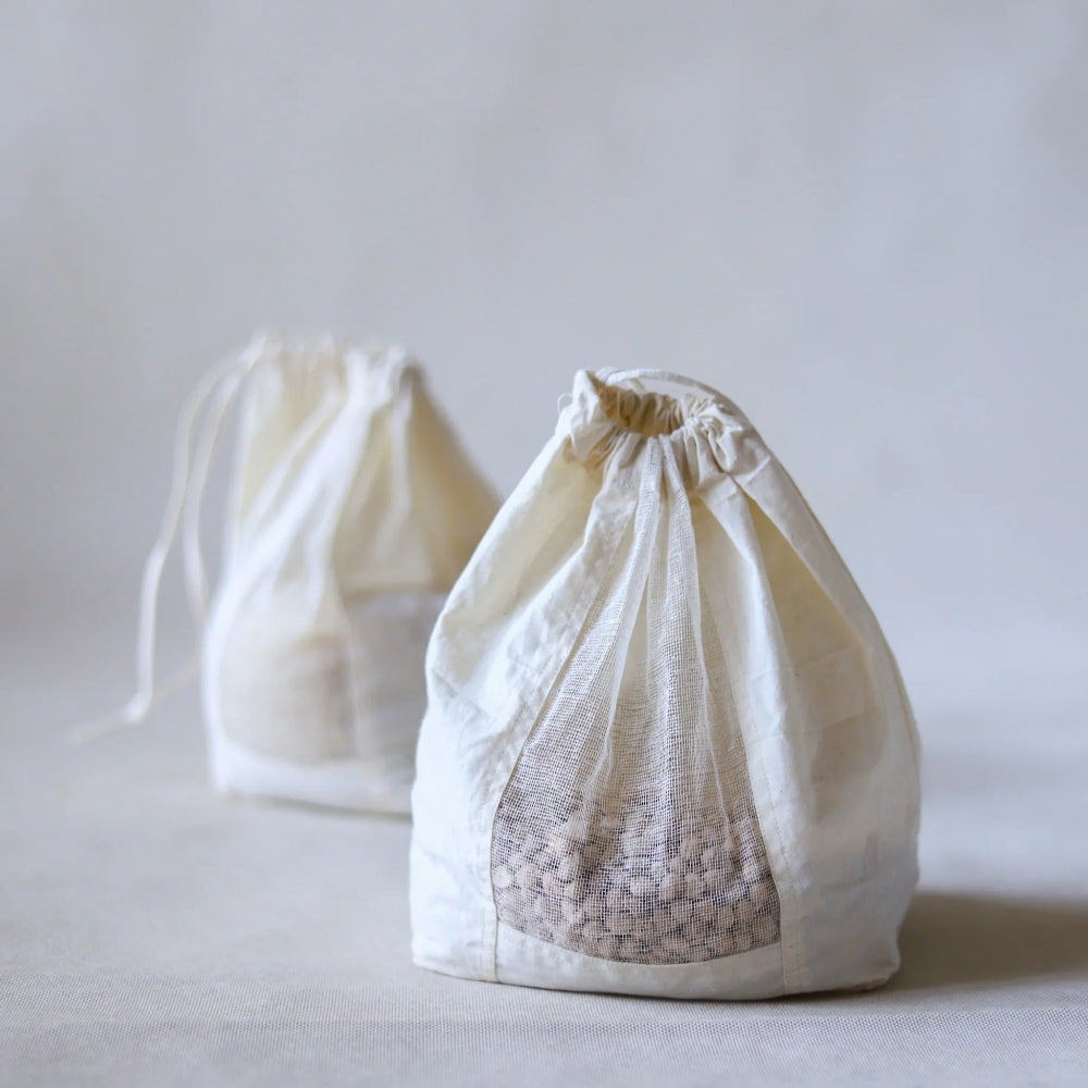 Two white organic cotton grain storage drawstring bags on a light grey background