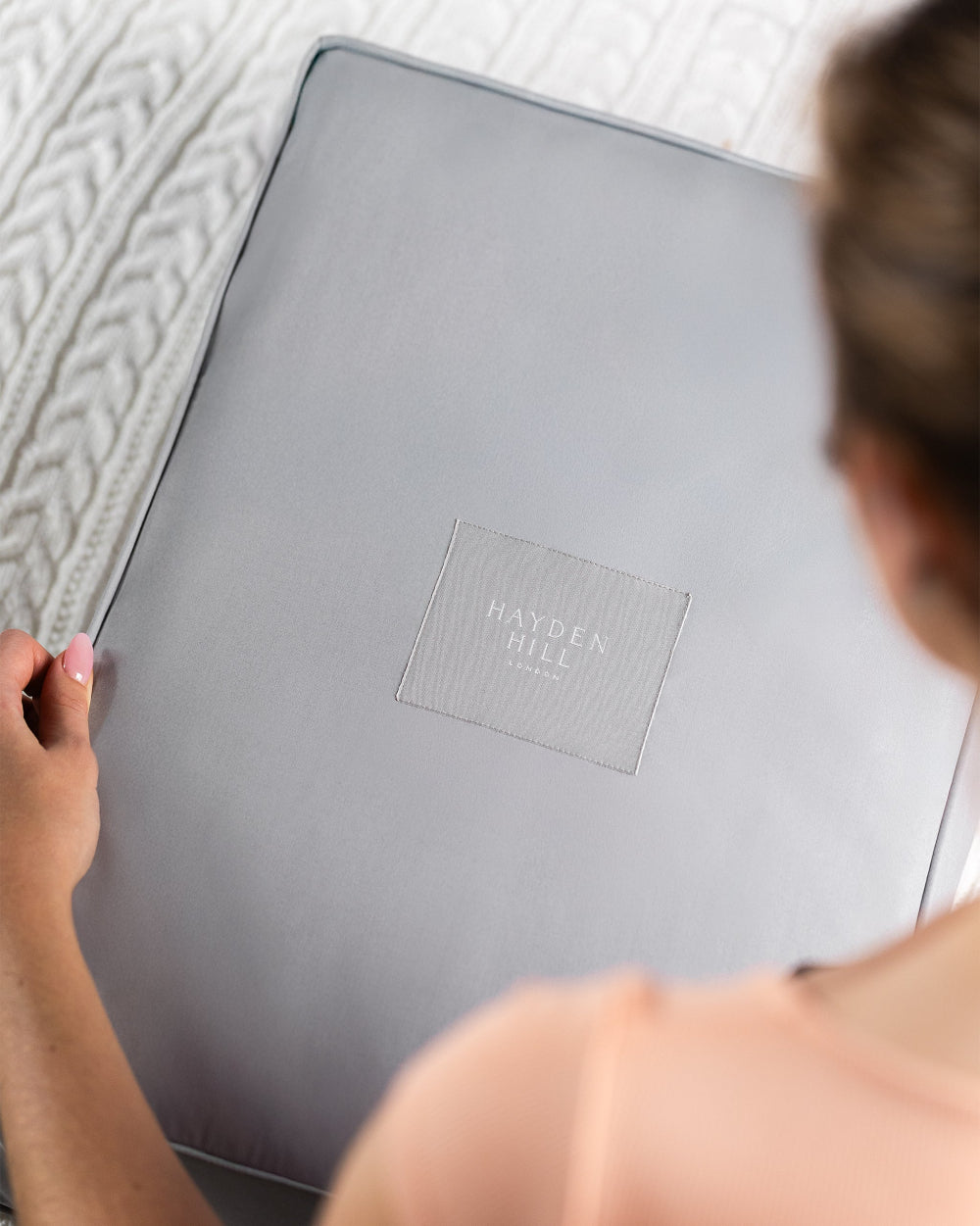 Person holding a grey organic storage bag with 'Hayden Hill' branding on a textured surface