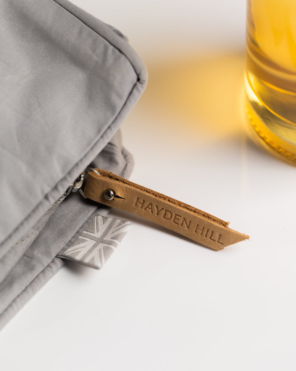 Grey pouch with a brown leather tag displaying 'Hayden Hill' on a light background.