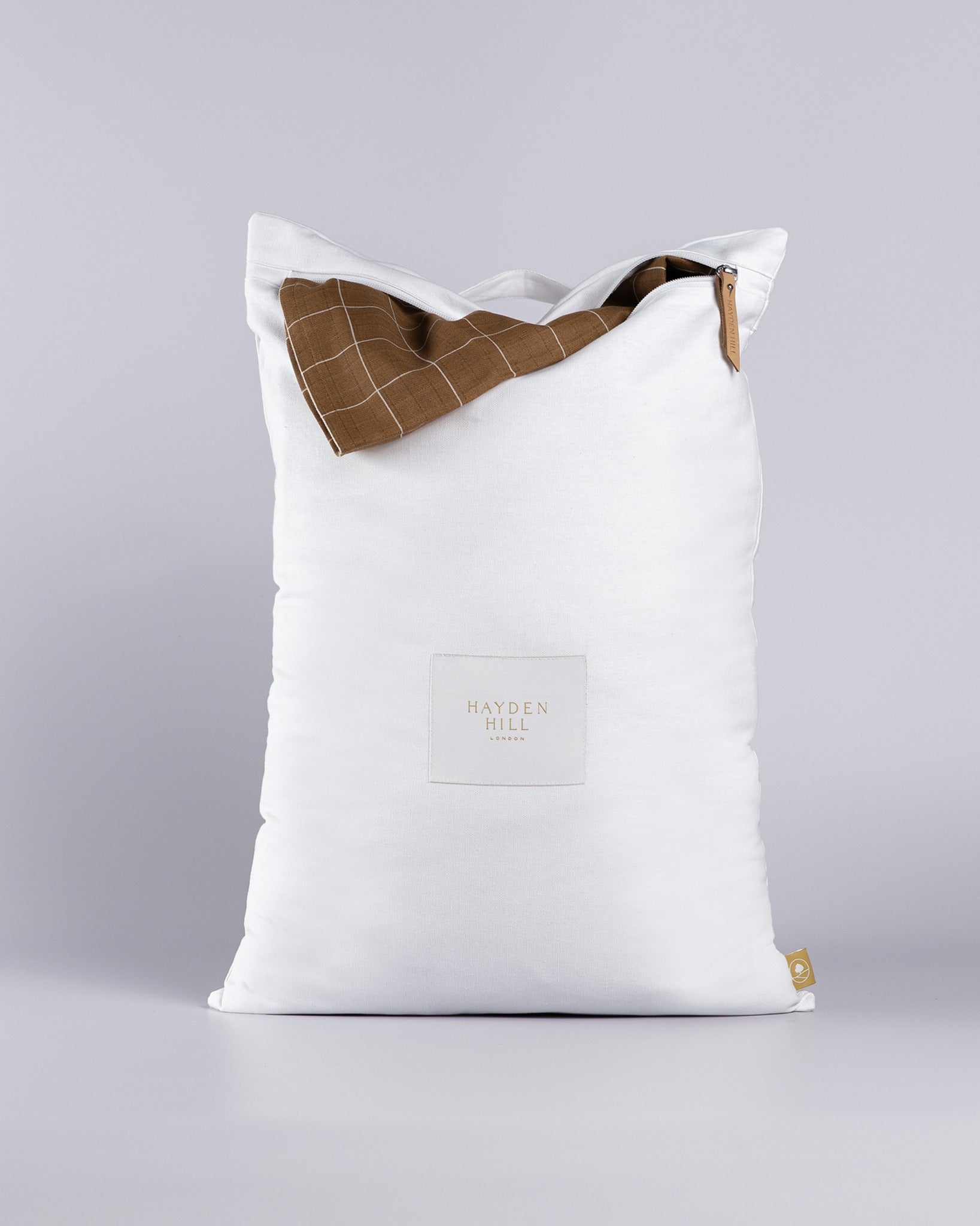 White travel laundry bag for dirty clothes with brown checkered clothes on a grey background