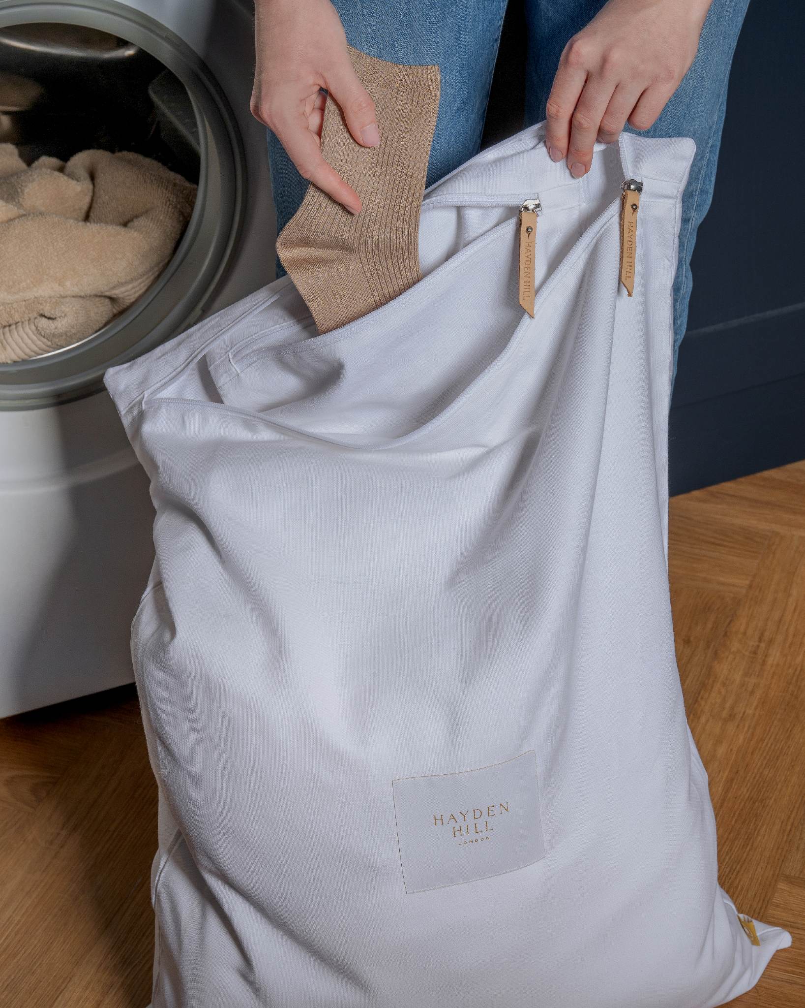 Person placing a sock into a laundry bag next to a washing machine.