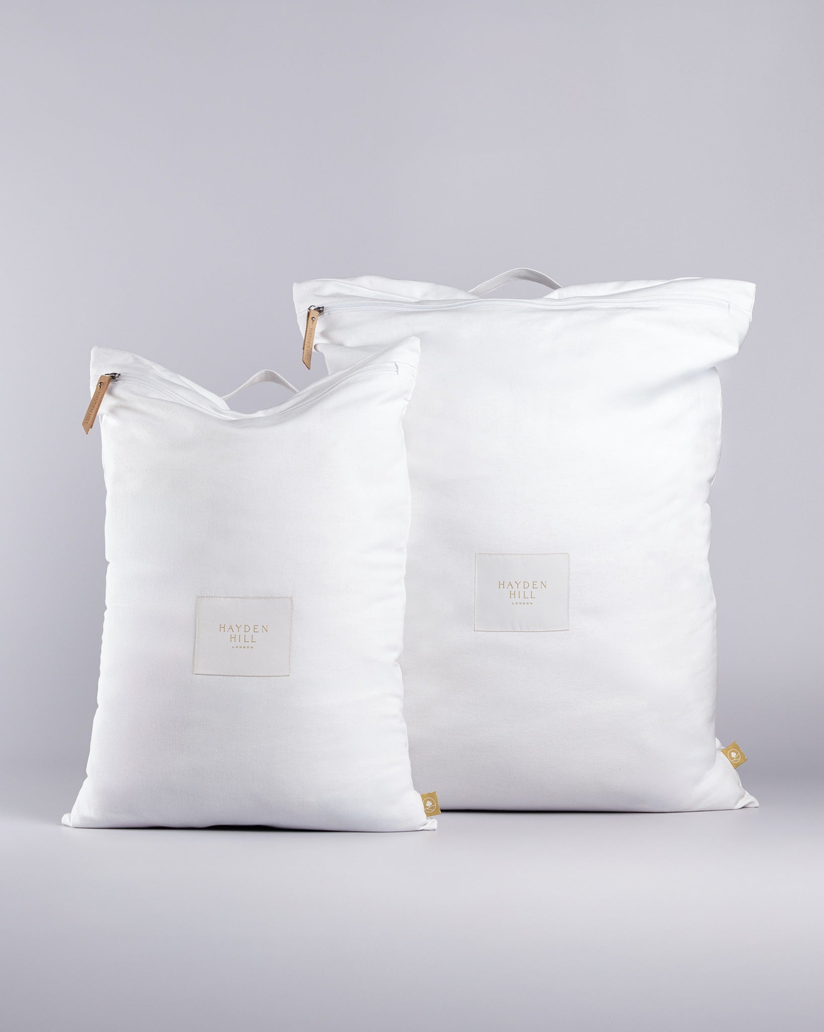 Two white organic travel laundry bags with leather zipper accents on a grey background