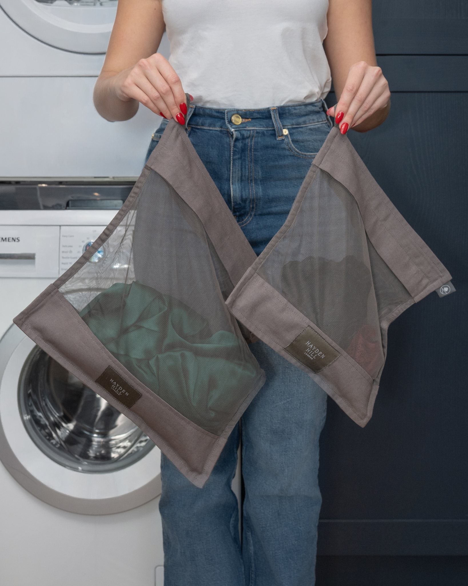 Person holding a mesh laundry bag with clothes inside in front of a washing machine.