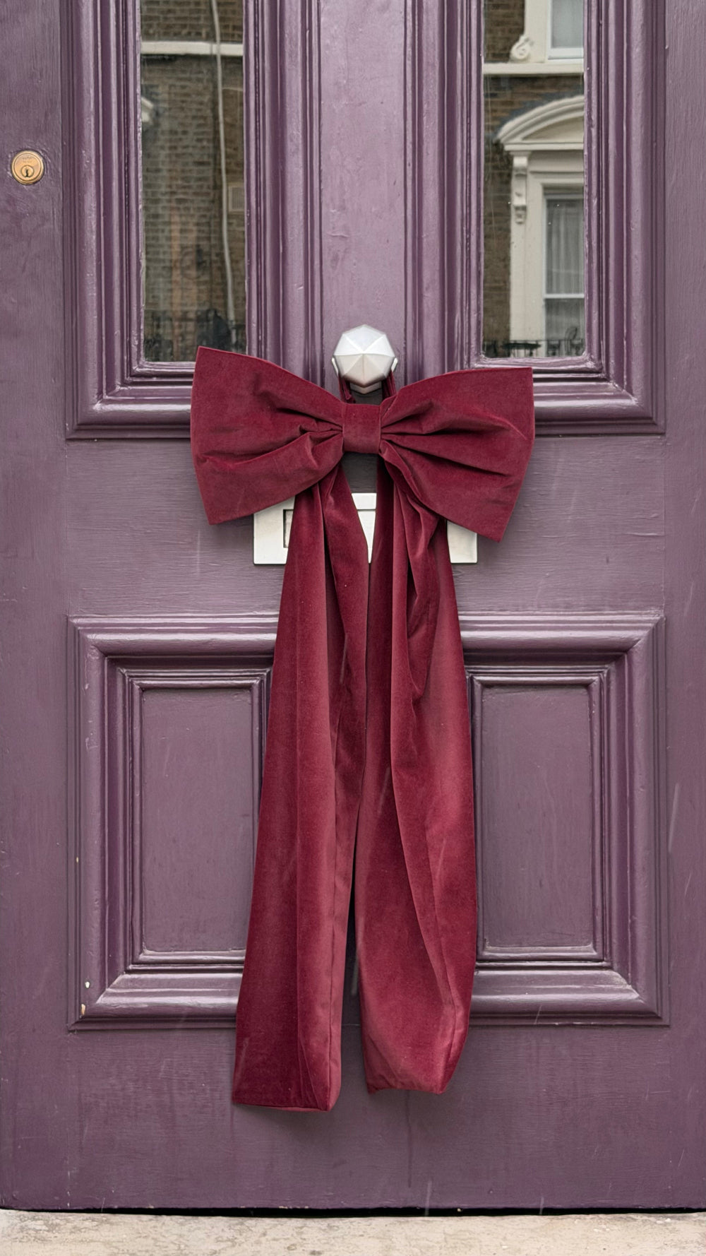 Kika Bespoke oversized burgundy velvet Christmas bow displayed on an indoor door