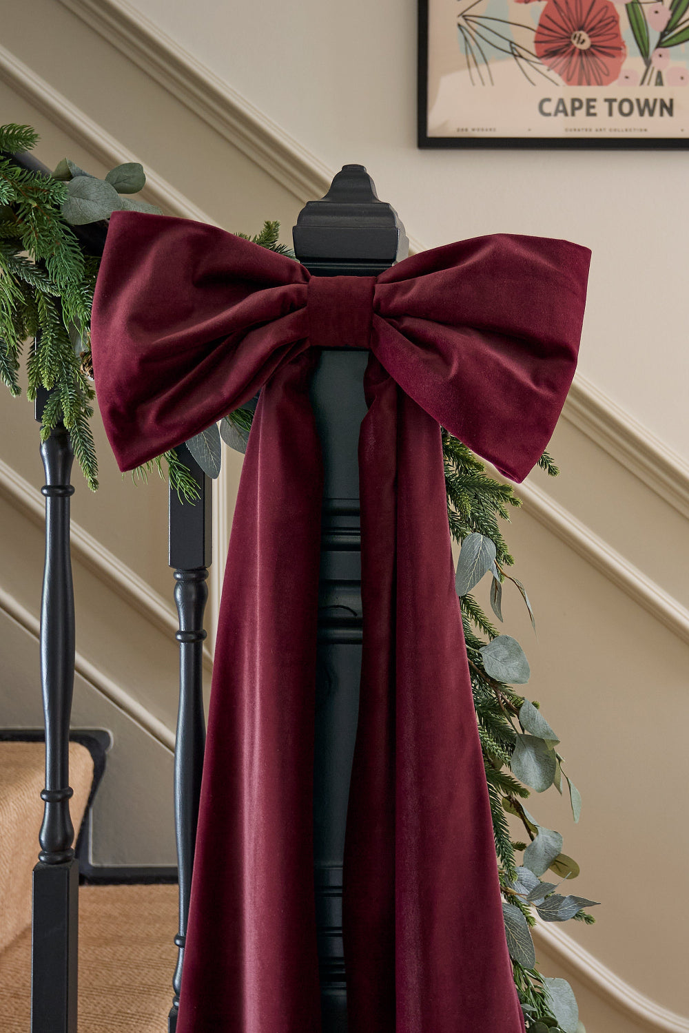 Oversized burgundy velvet bow decorating a staircase for Christmas