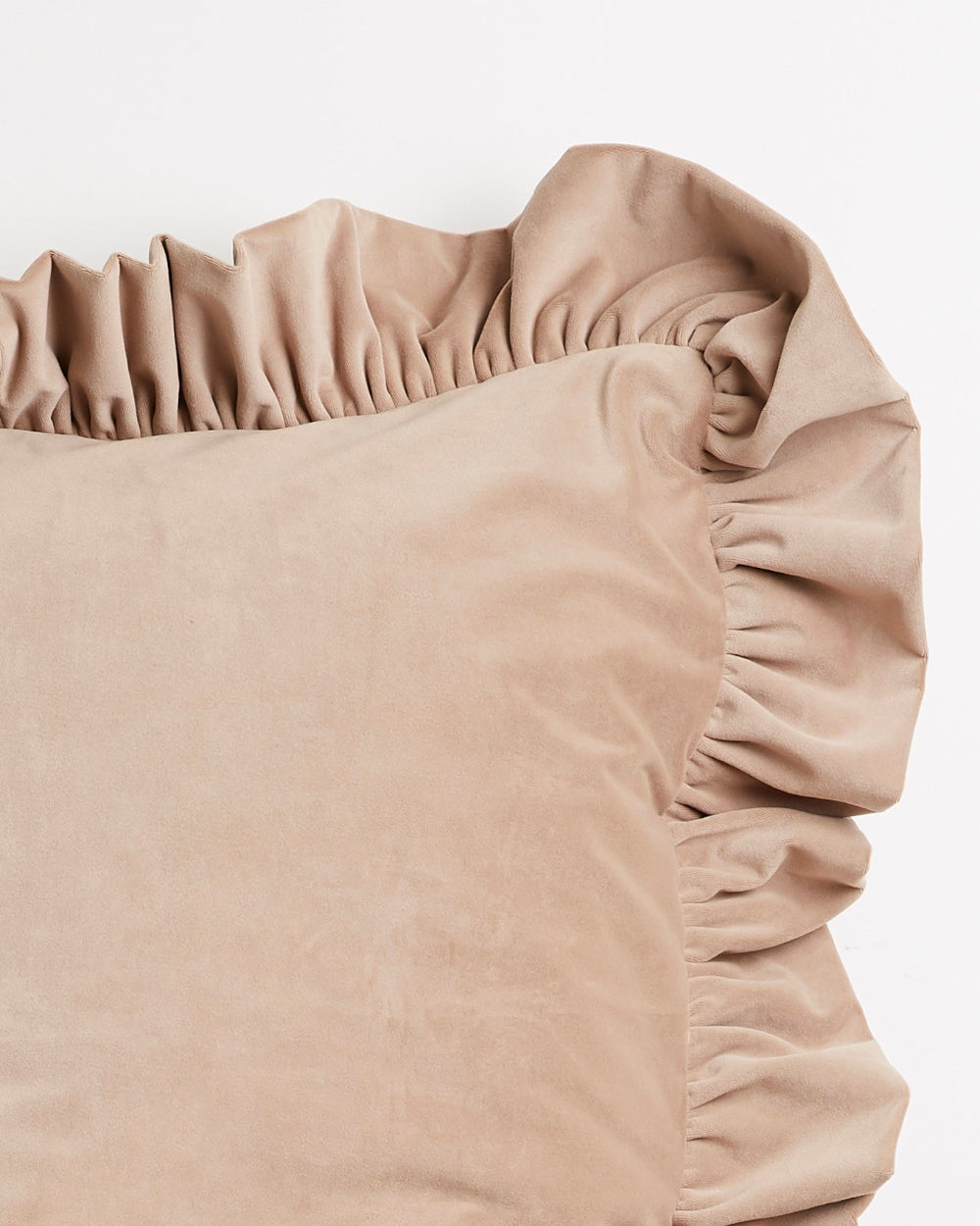 A close-up of a beige velvet pillow with a ruffled fabric trim, shown against a plain white background.