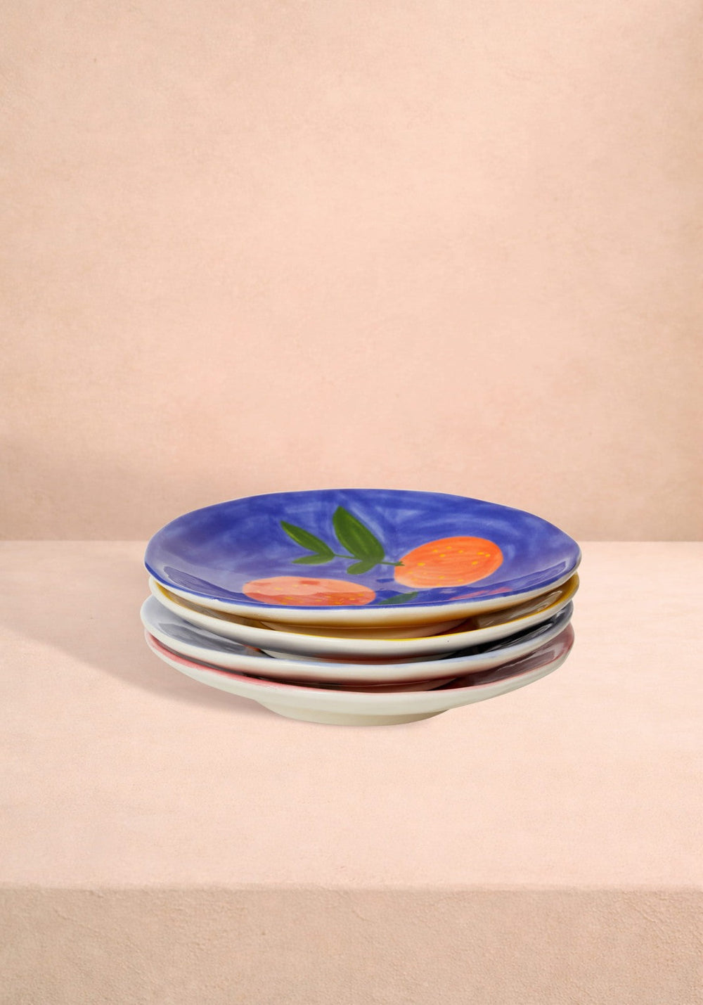 Stack of colourful ceramic plates with fruit design on a beige background