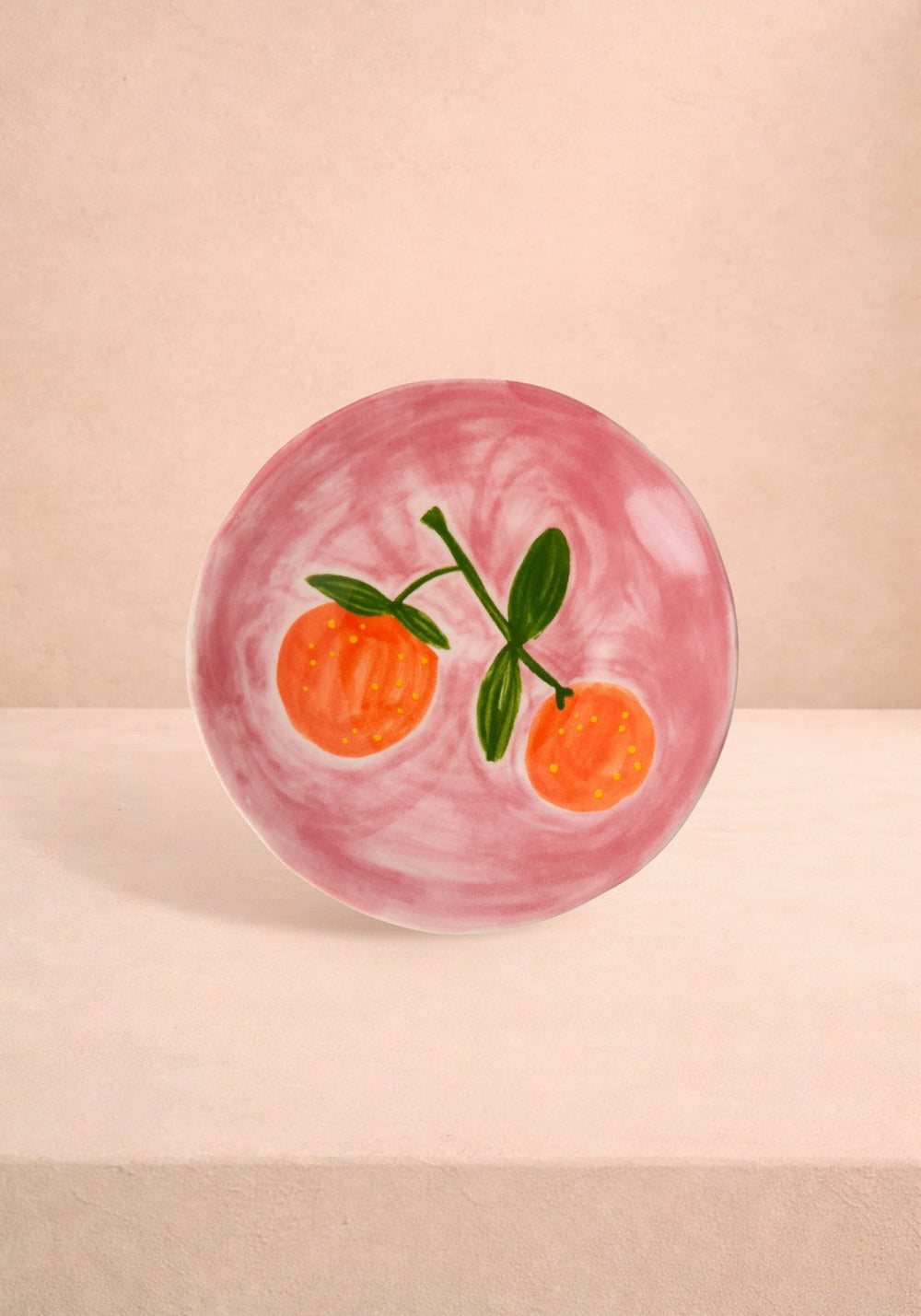 Pink ceramic plate with orange and green design on a beige background