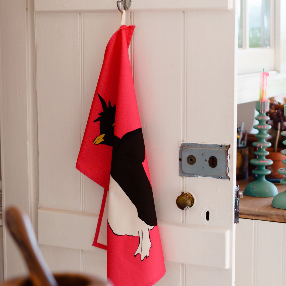 Pink Tea Towel with a black and white penguin design hanging on a hook.