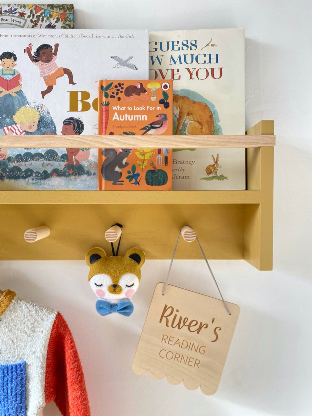 Wooden shelf with children's books and a sign indicating a reading corner, on a white wall.