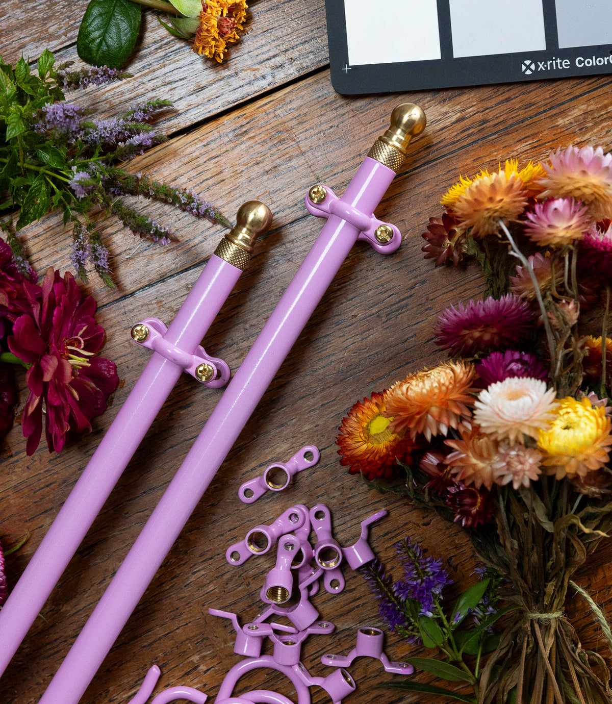 Kitchen mounting hardware, arranged on a rustic wooden surface surrounded by colourful flowers and a colour card.