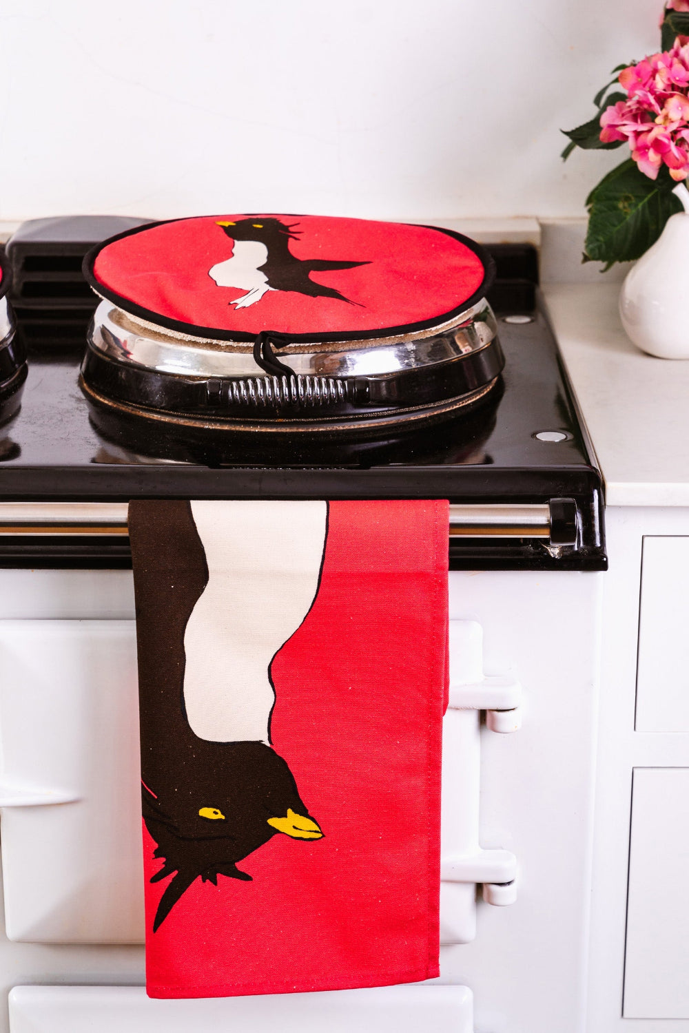 Pink tea towel with penguin design hanging on a stove handle in a kitchen.