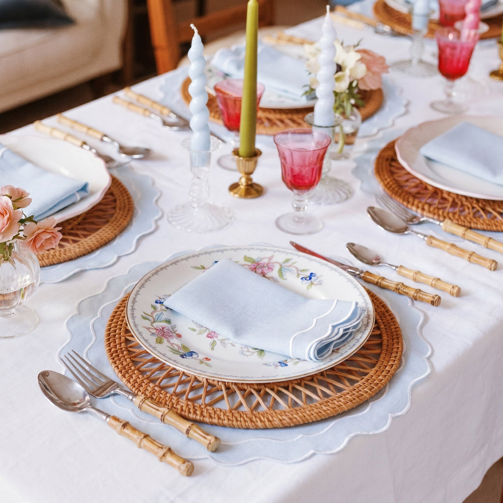 Elegant table setting with floral plates, wicker chargers, and red glasses.