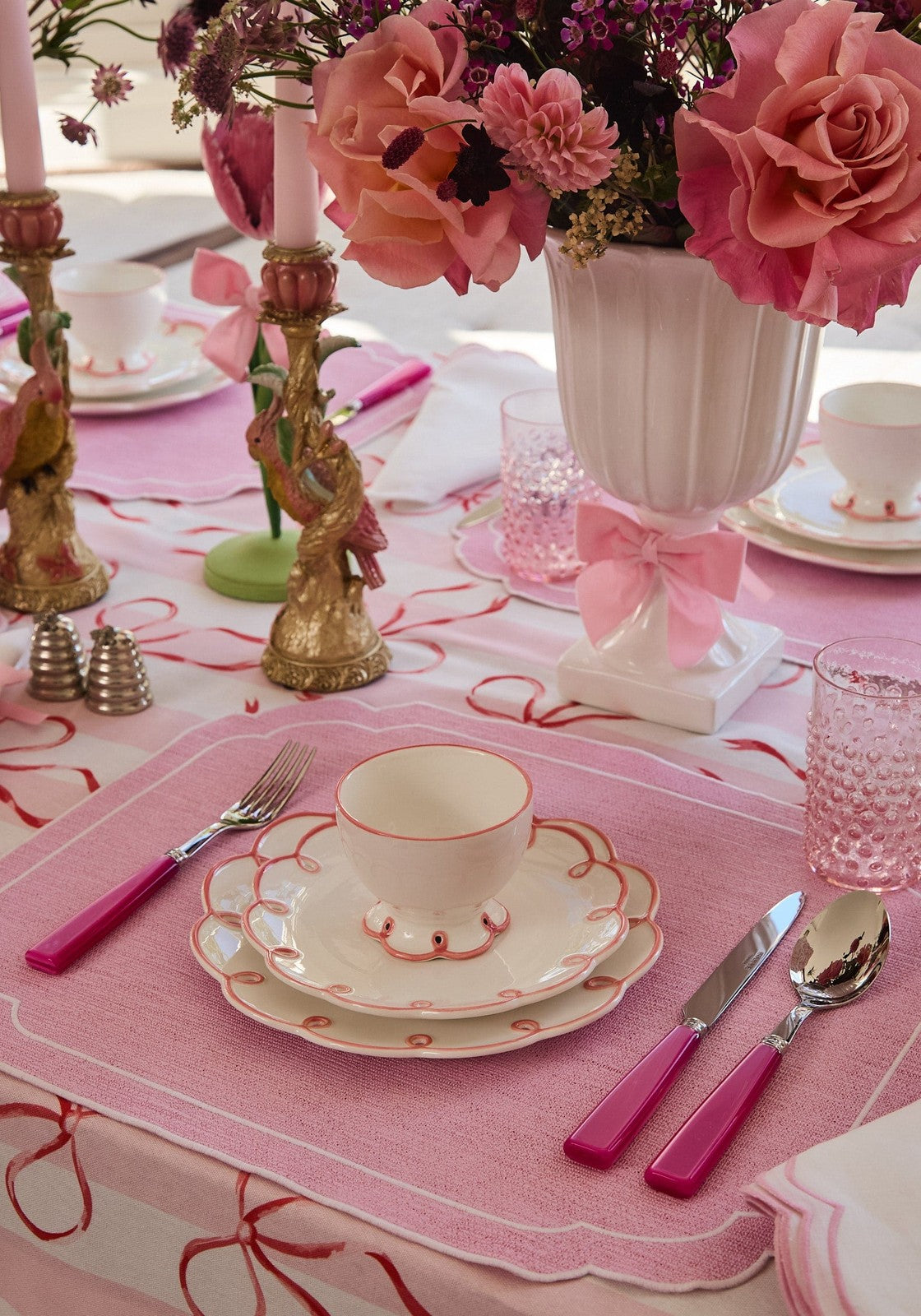 Elegant table setting with pink floral arrangement, teacup, and decorative elements on a pink tablecloth.
