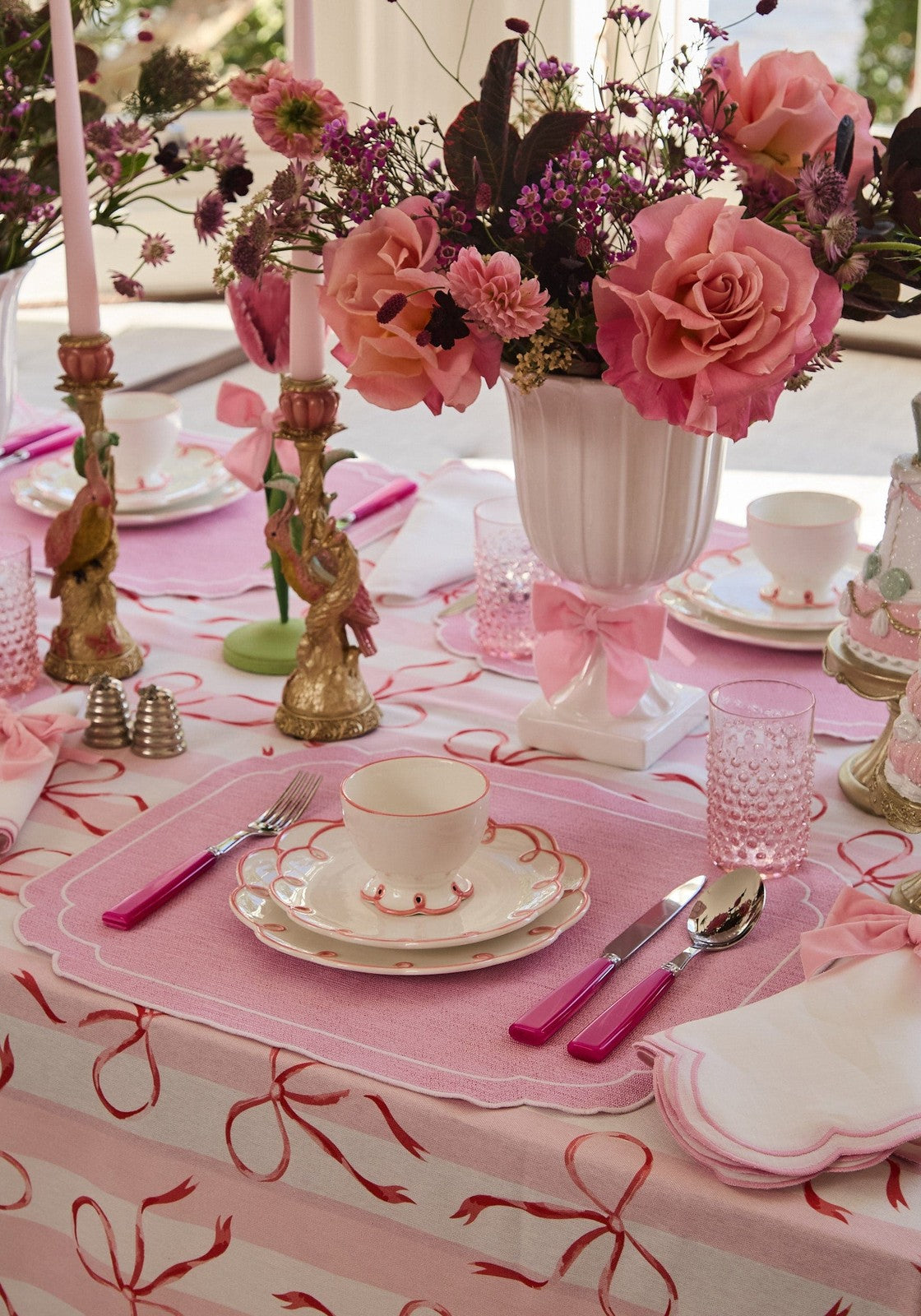 Decorative table setting with pink tablecloth, floral centerpieces, and tea cups.