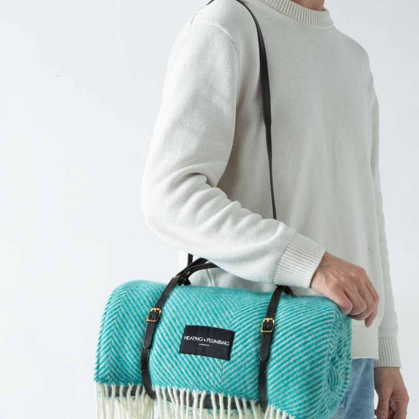 Person holding a turquoise picnic blanket with a brand label against a white background