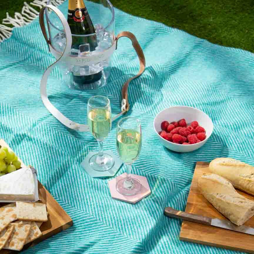 Picnic setup with champagne, raspberries, bread, and cheese on a turquoise blanket.