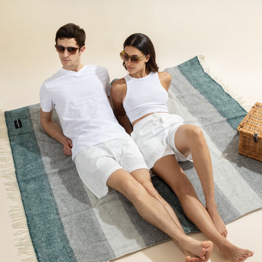 Two people sitting on a striped blanket with a picnic basket in the background