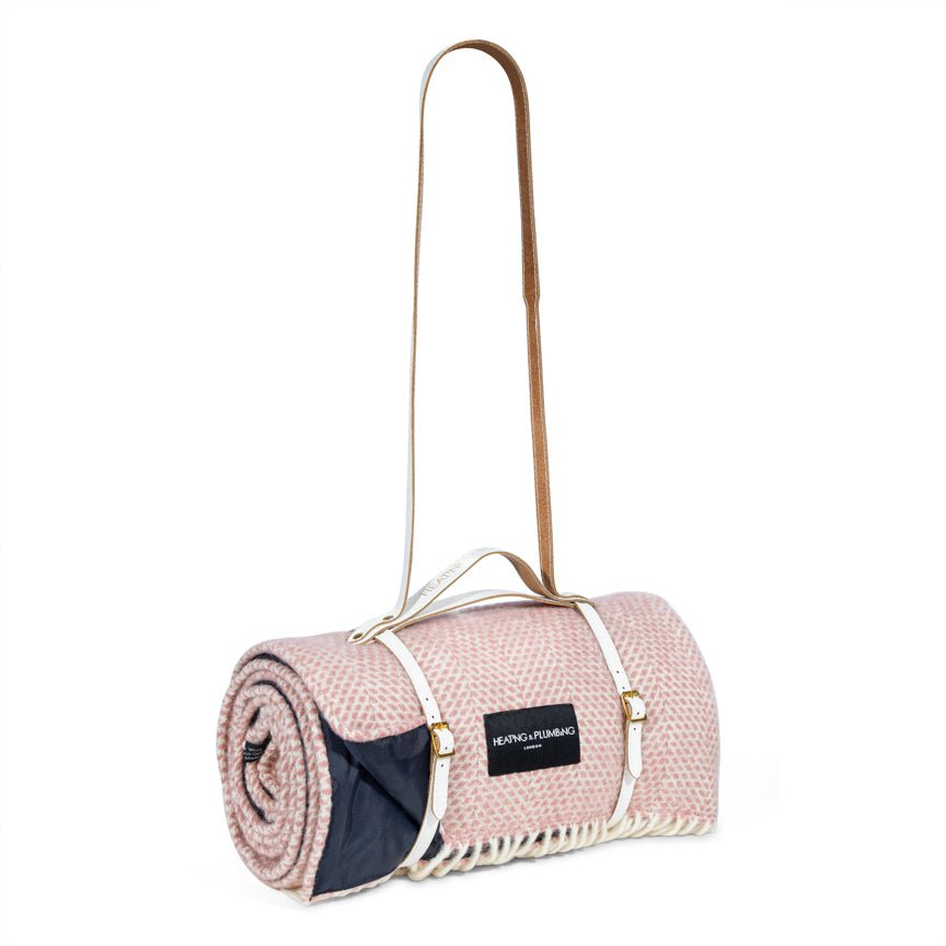 Pink picnic blanket with carrying strap on a white background