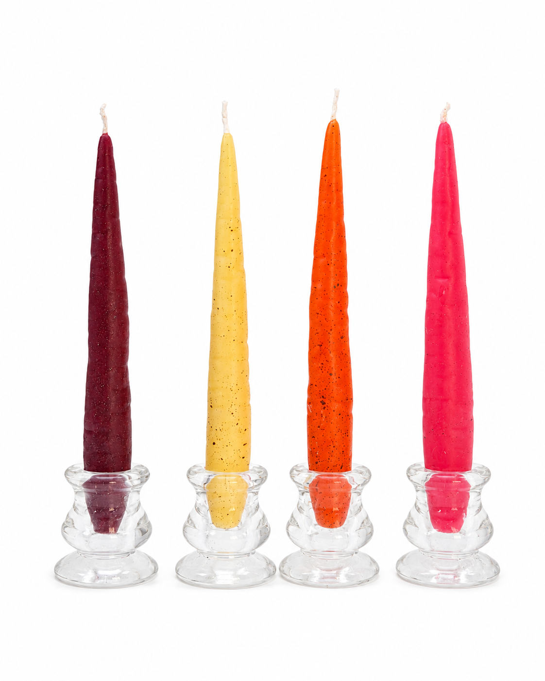 Four colourful carrot-shaped beeswax candles in burgundy, yellow, orange and pink displayed in clear glass candle holders.