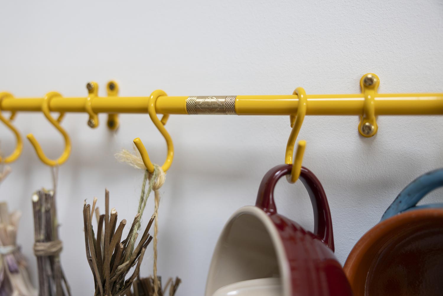 Yellow wall-mounted hanging rack with multiple hooks, shown holding several mugs against a plain light wall.
