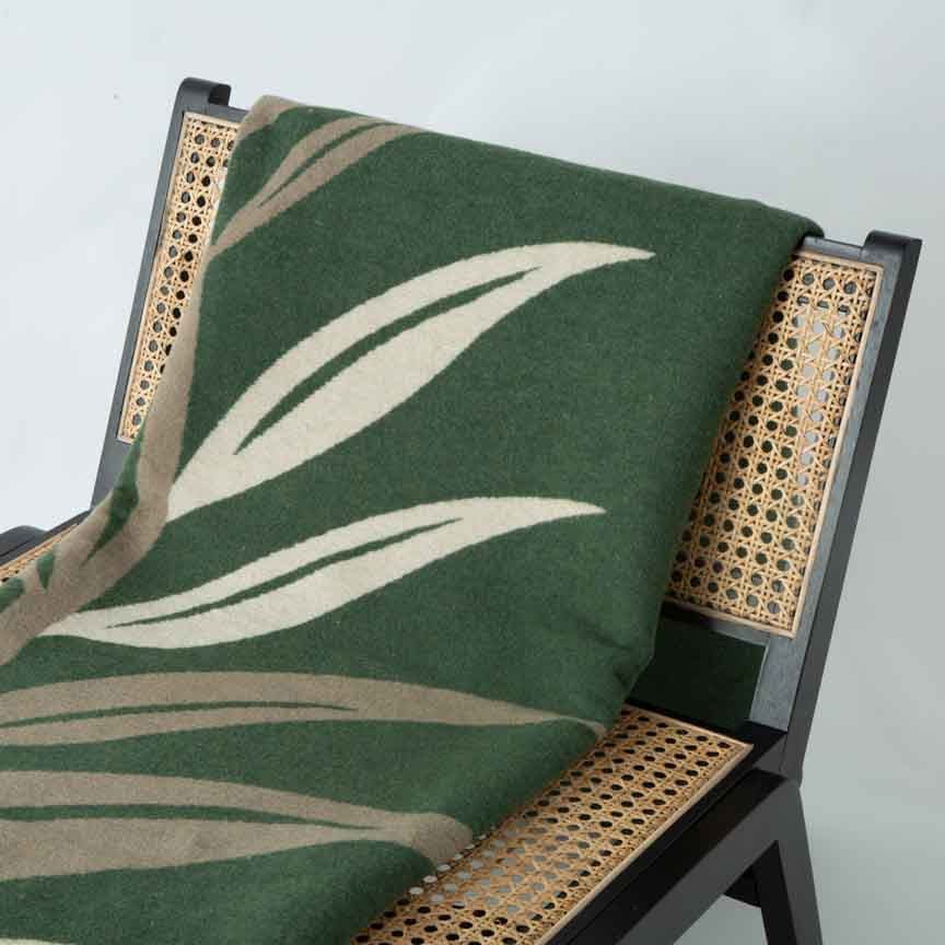 Green leaf-patterned blanket draped over a wicker chair against a light grey background