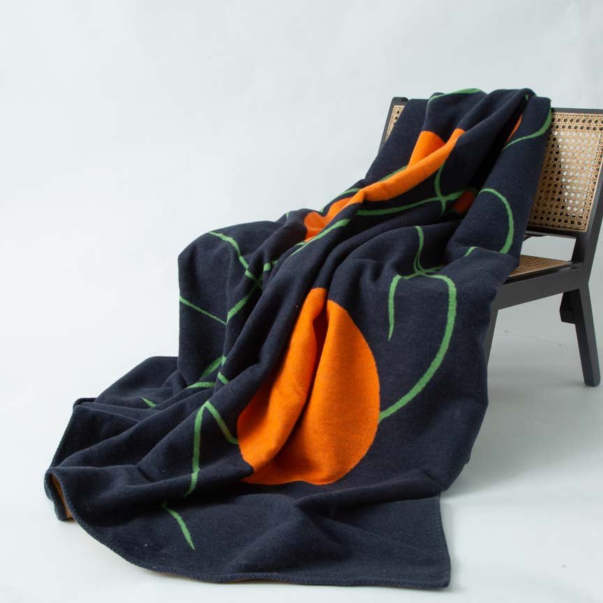 Black blanket with orange and green patterns draped over a chair on a white background