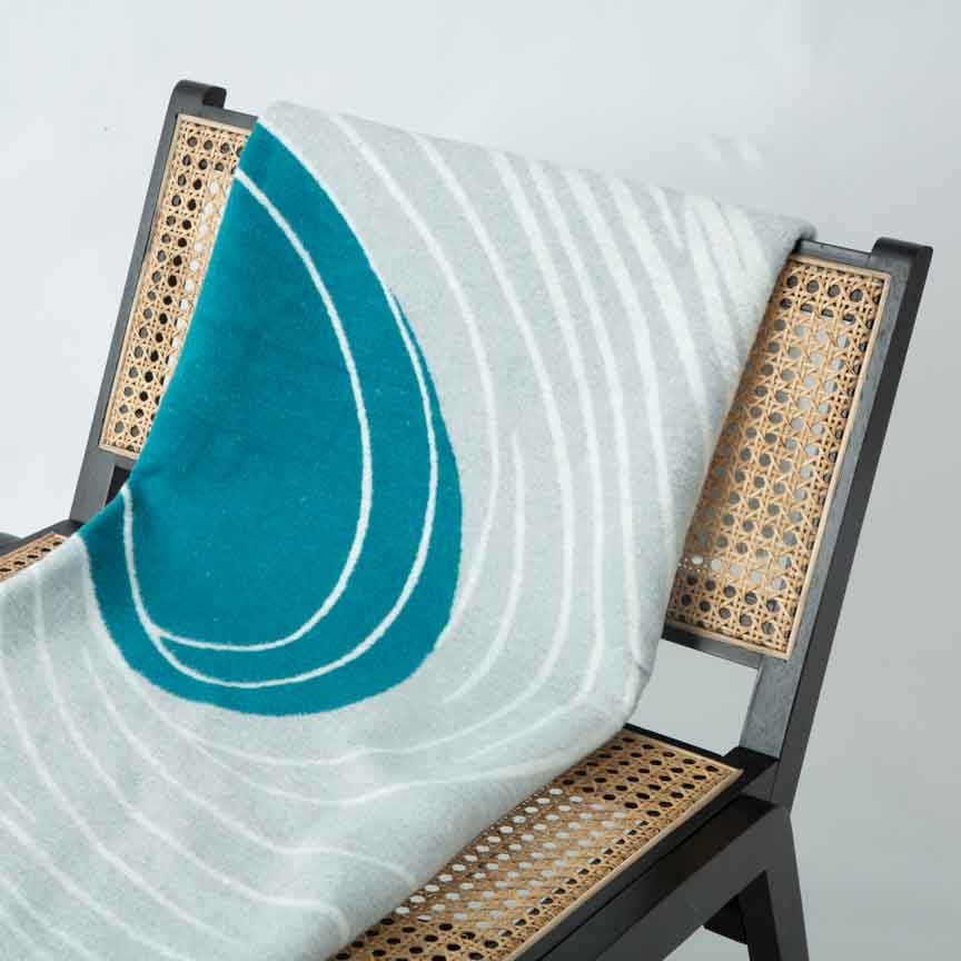 Teal and white patterned blanket draped over a chair with wicker backrest.