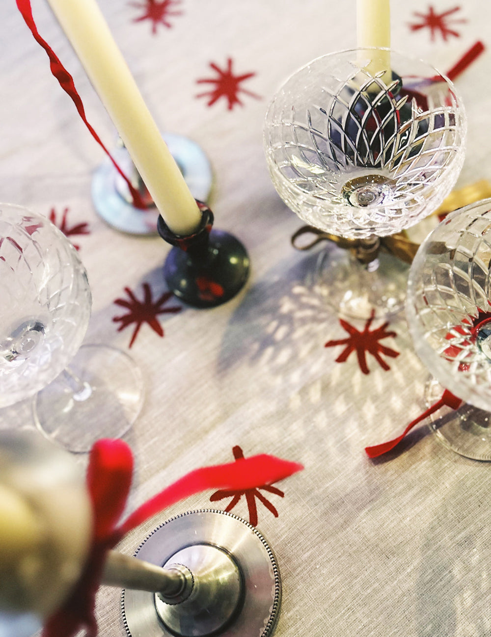 Decorative table setting with glasses, candles, and an ornament on a patterned tablecloth.