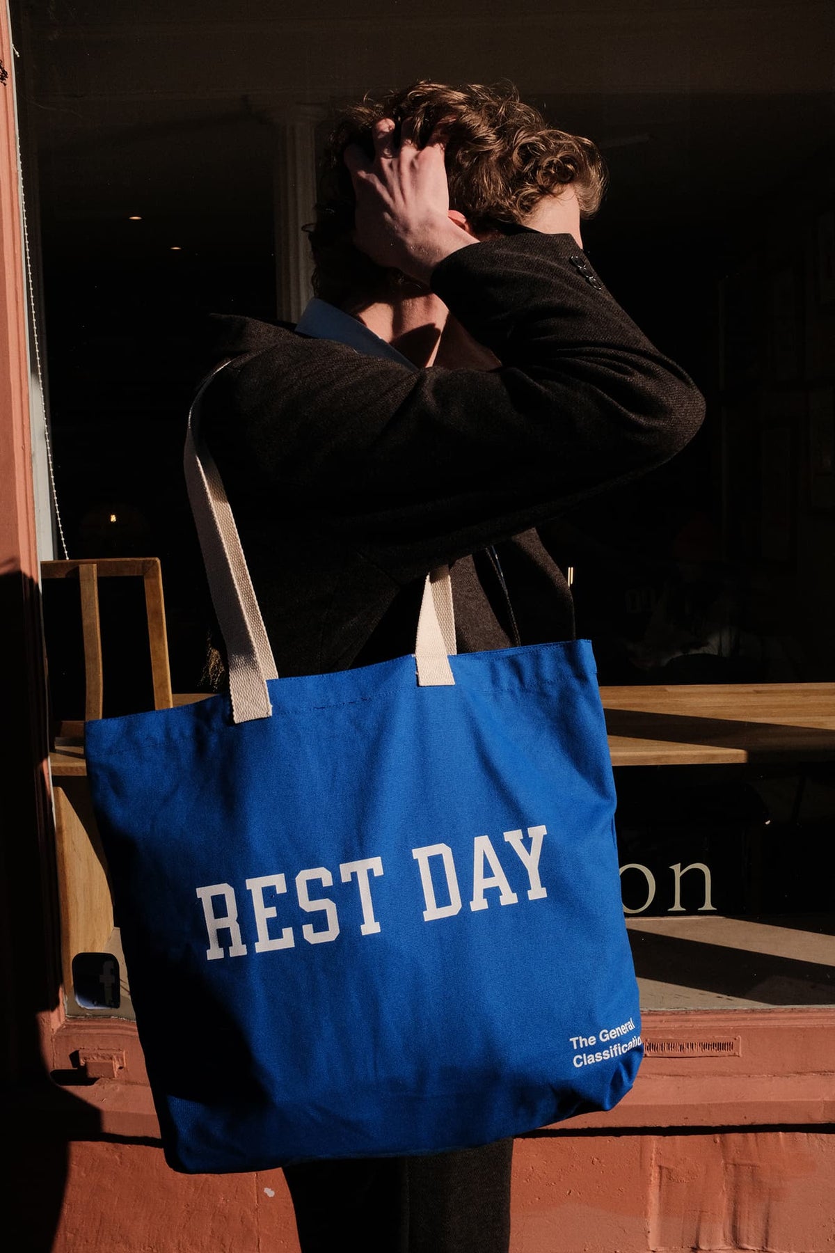 Person holding a blue tote bag with 'REST DAY' text against a dark background
