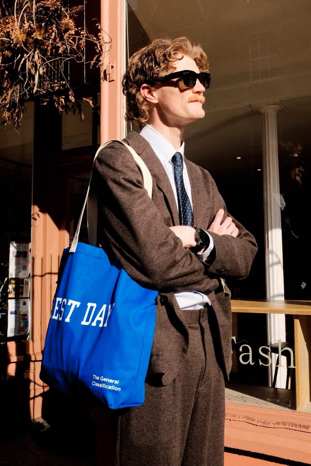 Man in a suit with a blue bag reading 'Rest Day' standing outside a store.
