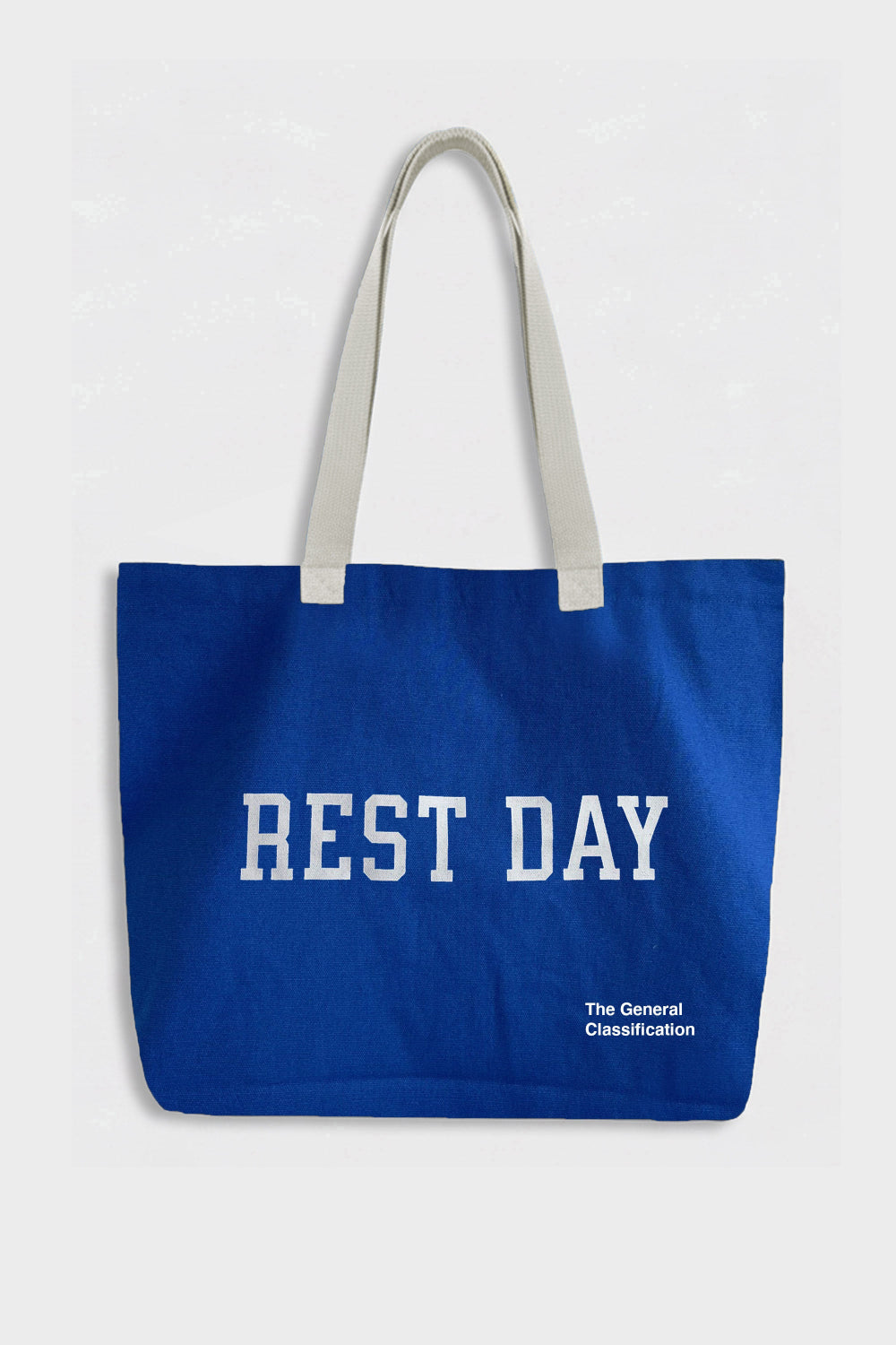 A blue canvas tote bag with white shoulder straps and white printed text reading 'REST DAY' and 'The General Classification' on a light grey background.