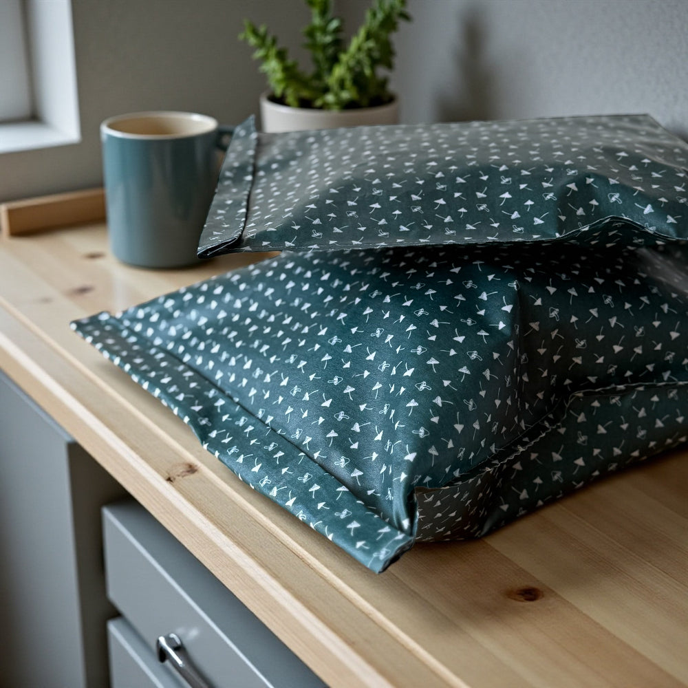 Green patterned reusable beeswax food bags on a wooden surface with a cup and plant in the background