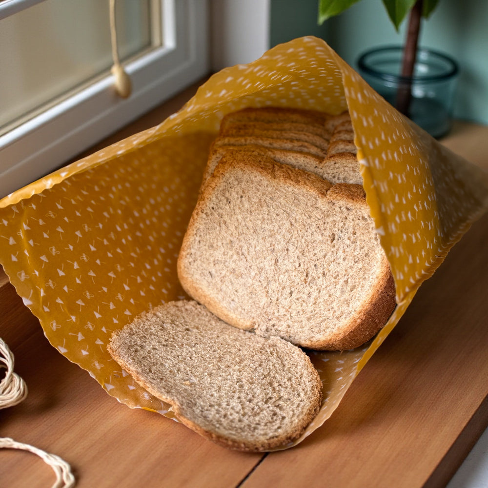 Sliced bread on in a yellow patterned beeswax wrap on a wooden surface