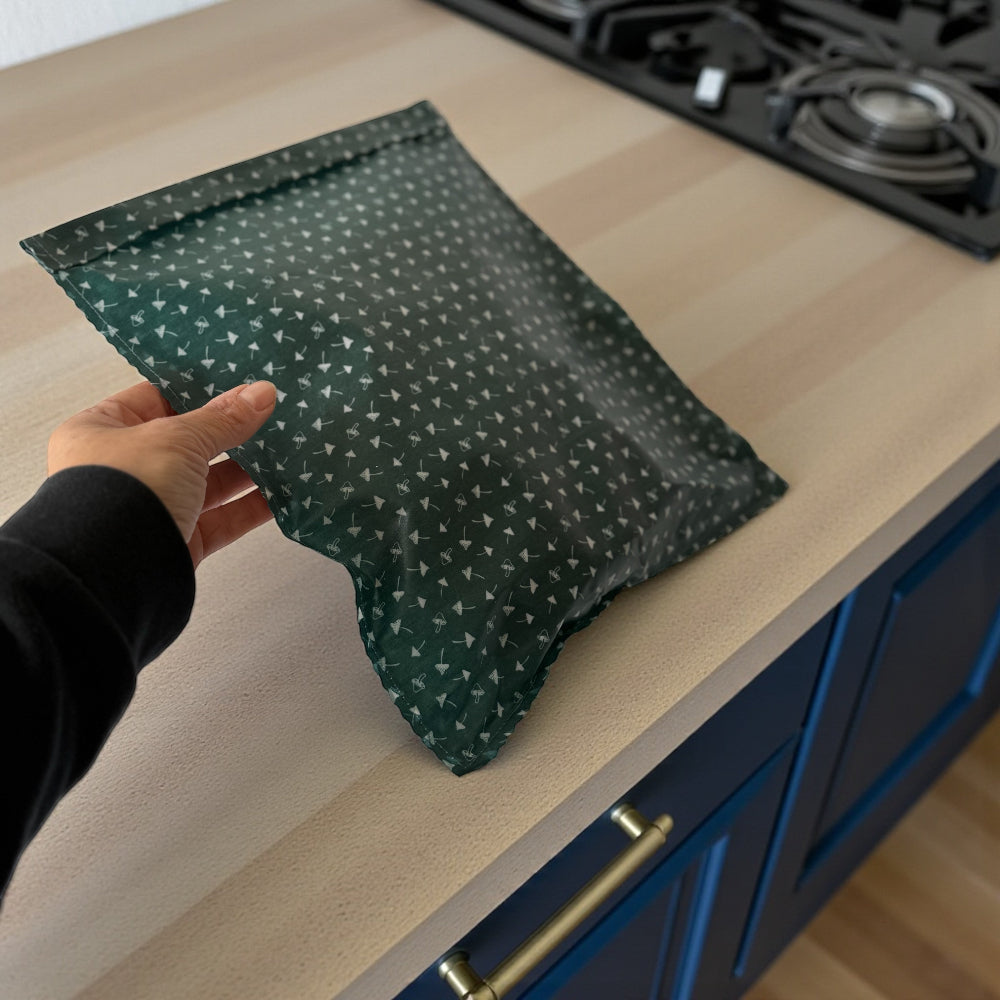 Green patterned toadstool beeswax wrap food bag held by a hand on a kitchen counter