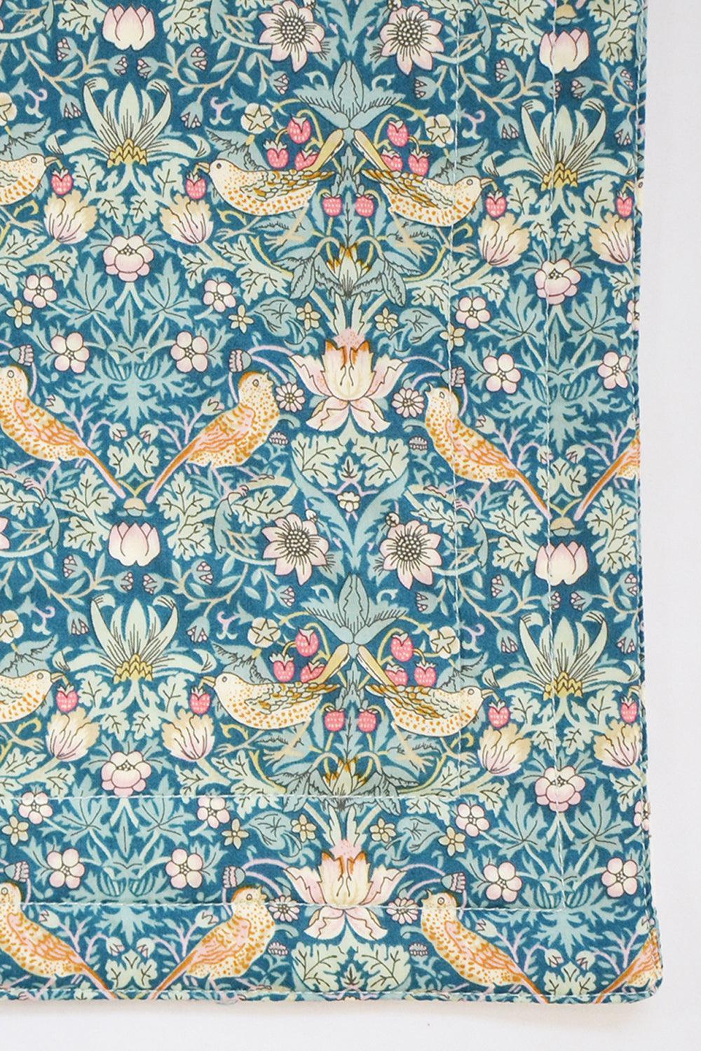 Patterned fabric placemat with birds and flowers on a blue background