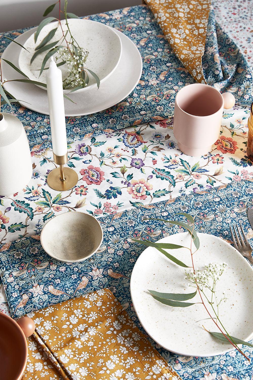 Table setting with Liberty floral tablecloth, plates, cups, and cutlery.