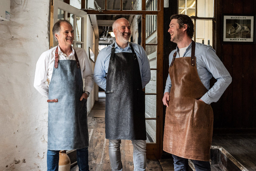 Three men wearing aprons standing in a rustic interior setting.