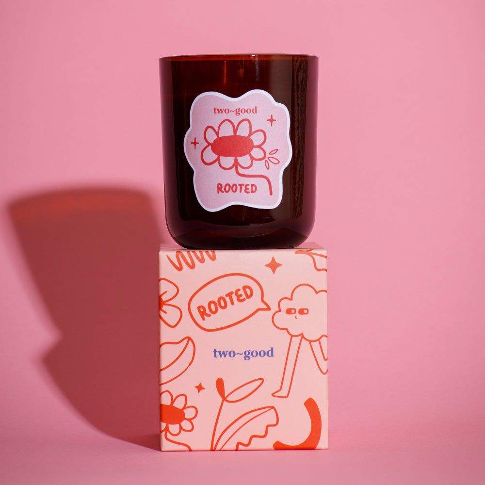 Brown candle with 'two-good' branding on a pink background