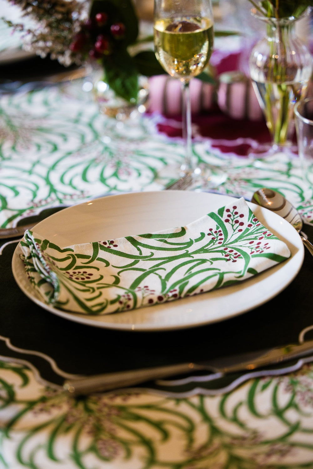 Rosie Dalia Winter Berries cotton napkin folded on a white plate at a festive dining table.