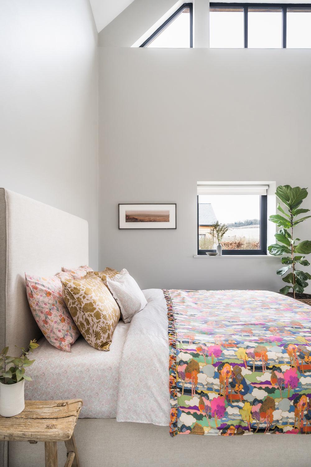 Modern bedroom with a bed, colourful blanket, and decorative pillows.