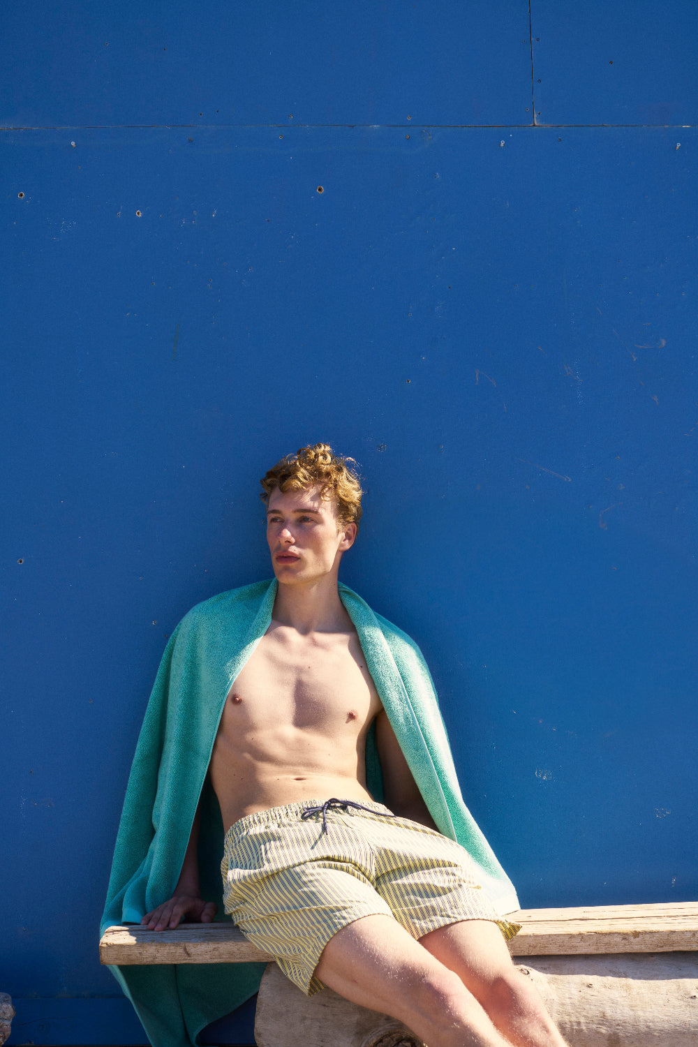 Man sitting on a bench against a blue wall with a sage green organic towel draped over his shoulder.