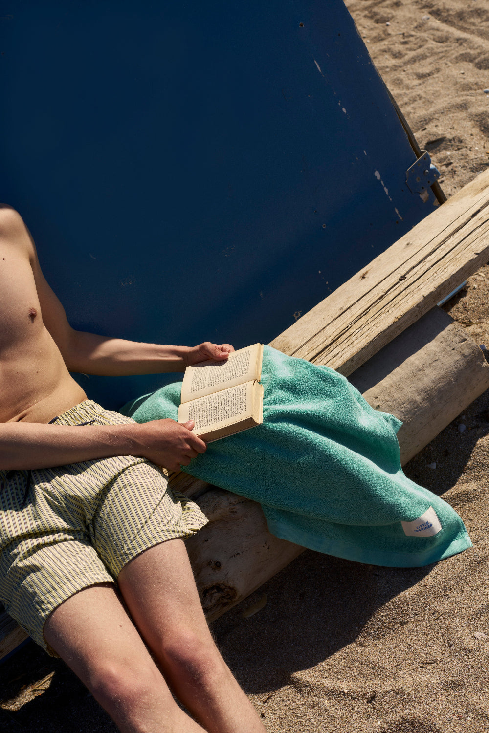 Man sitting on a wooden bench at the beach holding a book.