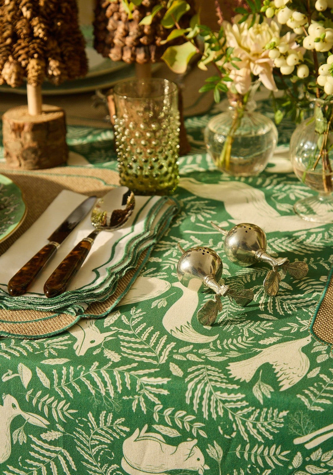 Christmas table setting with a green and white patterned tablecloth, silverware, and decorative elements.
