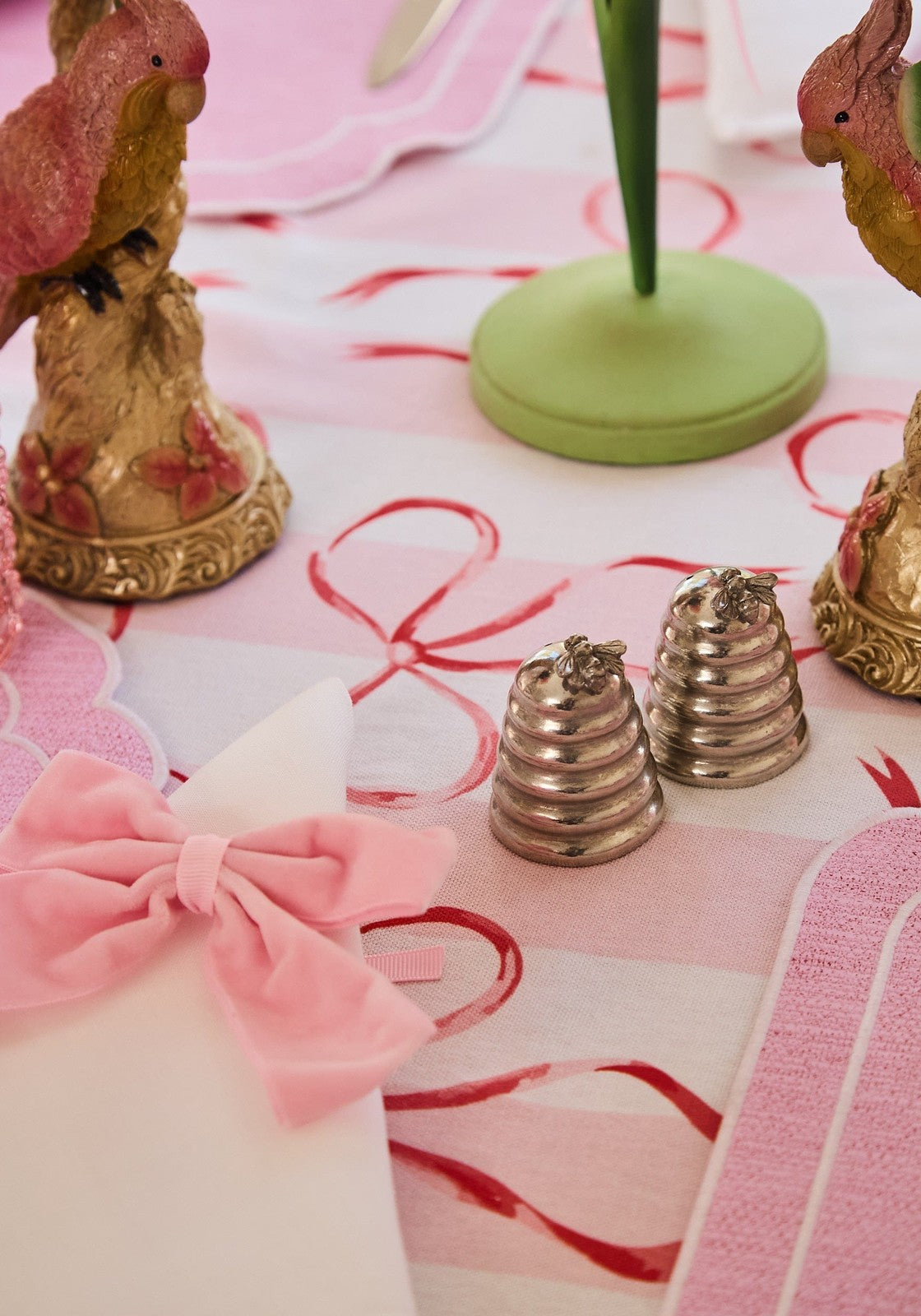 Decorative table setting with pink napkins, gold figurines, and a green holder on a pink tablecloth.