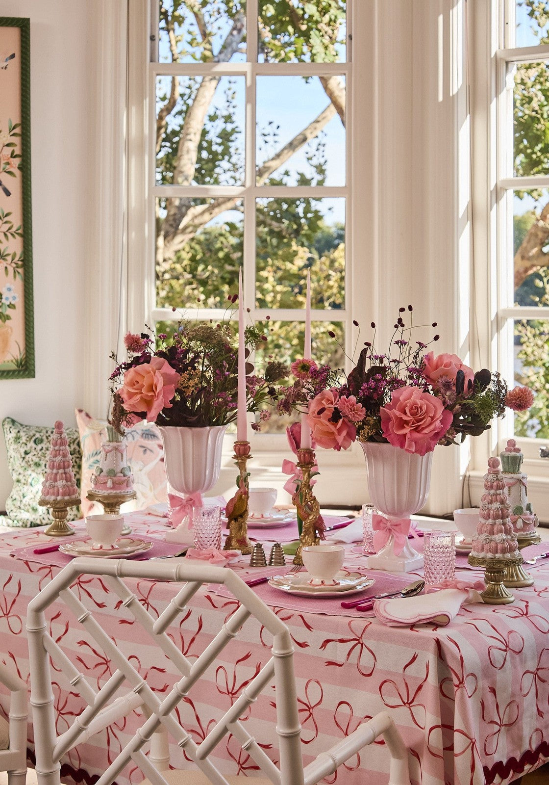 Elegant table setting with pink tablecloth and floral centerpieces in a bright room with large windows.
